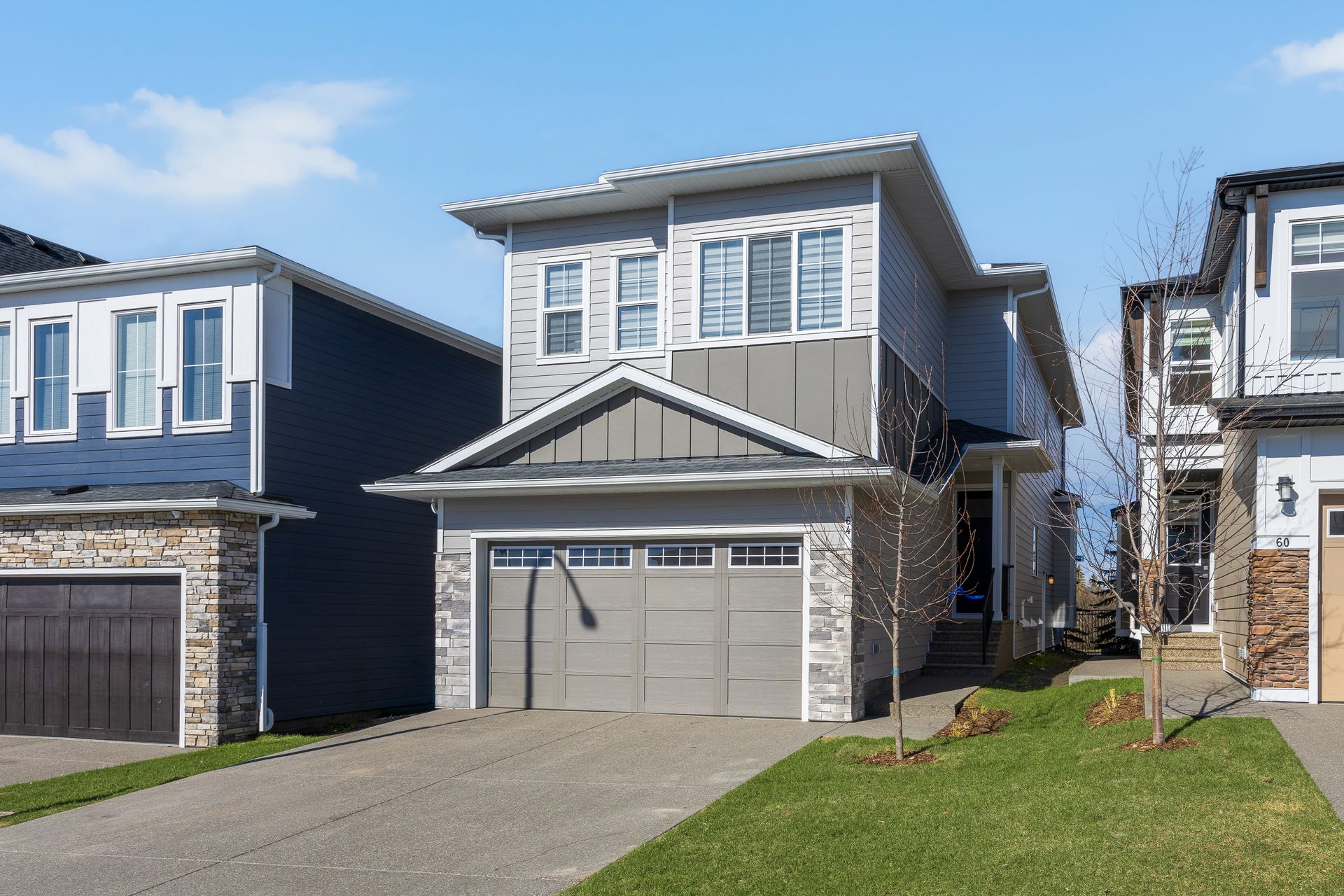 Suburban two-story house with gray garage doors, blue siding, and a driveway under bright sun