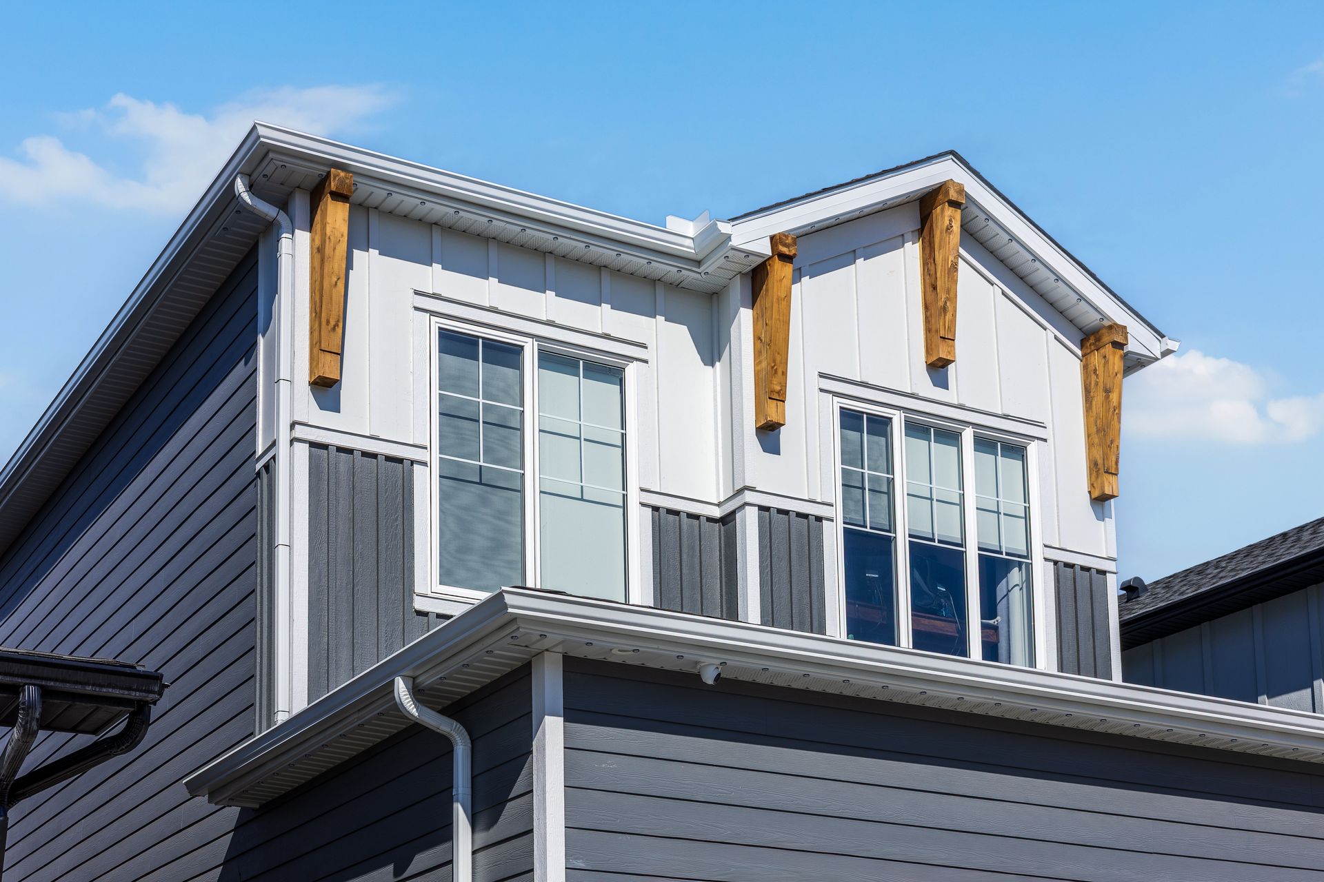 Modern two-story house exterior with gray siding, white trim, and dormer windows against a blue sky