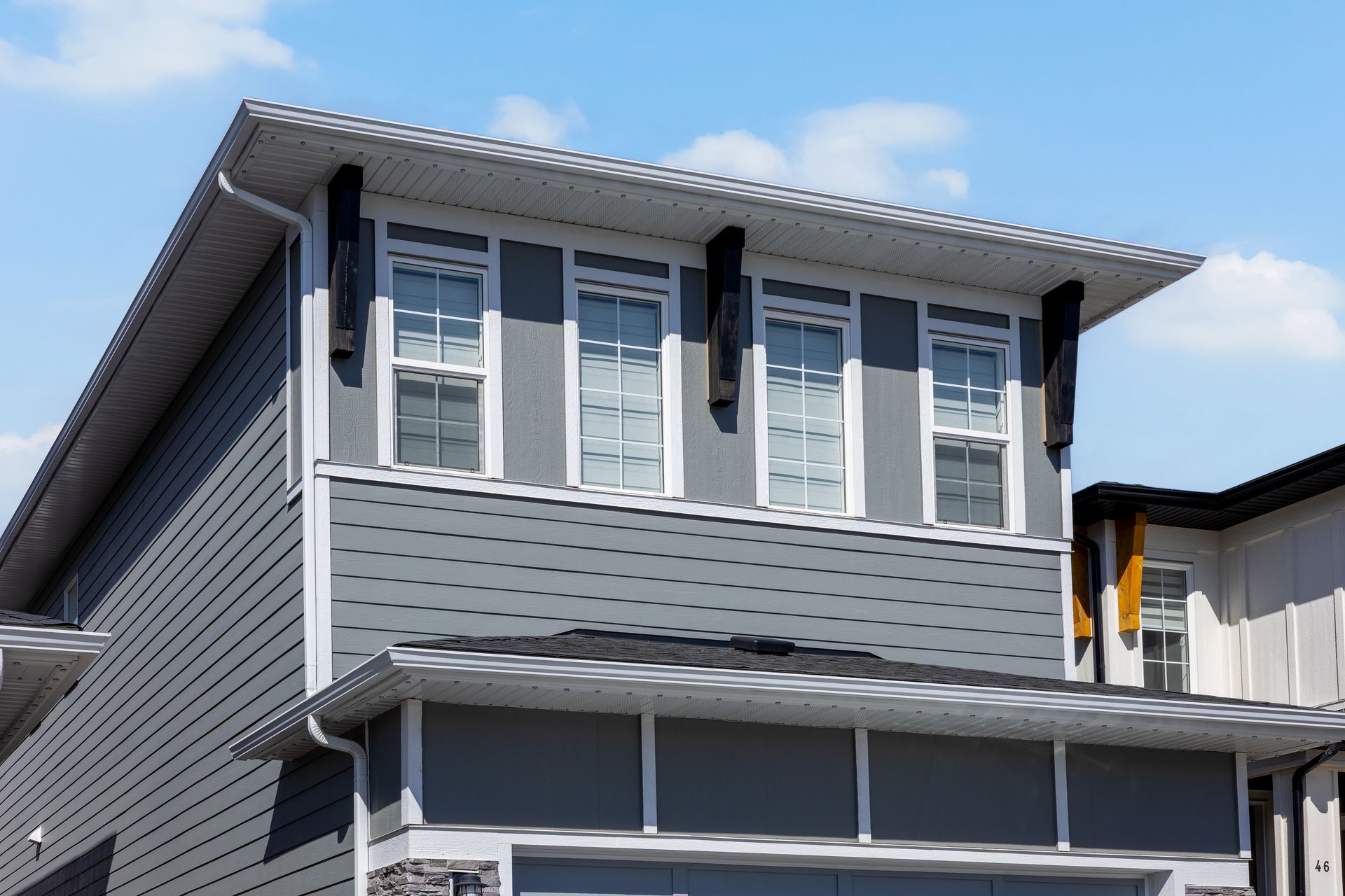 Gray two-story house exterior with white-trimmed windows and a balcony under a blue sky