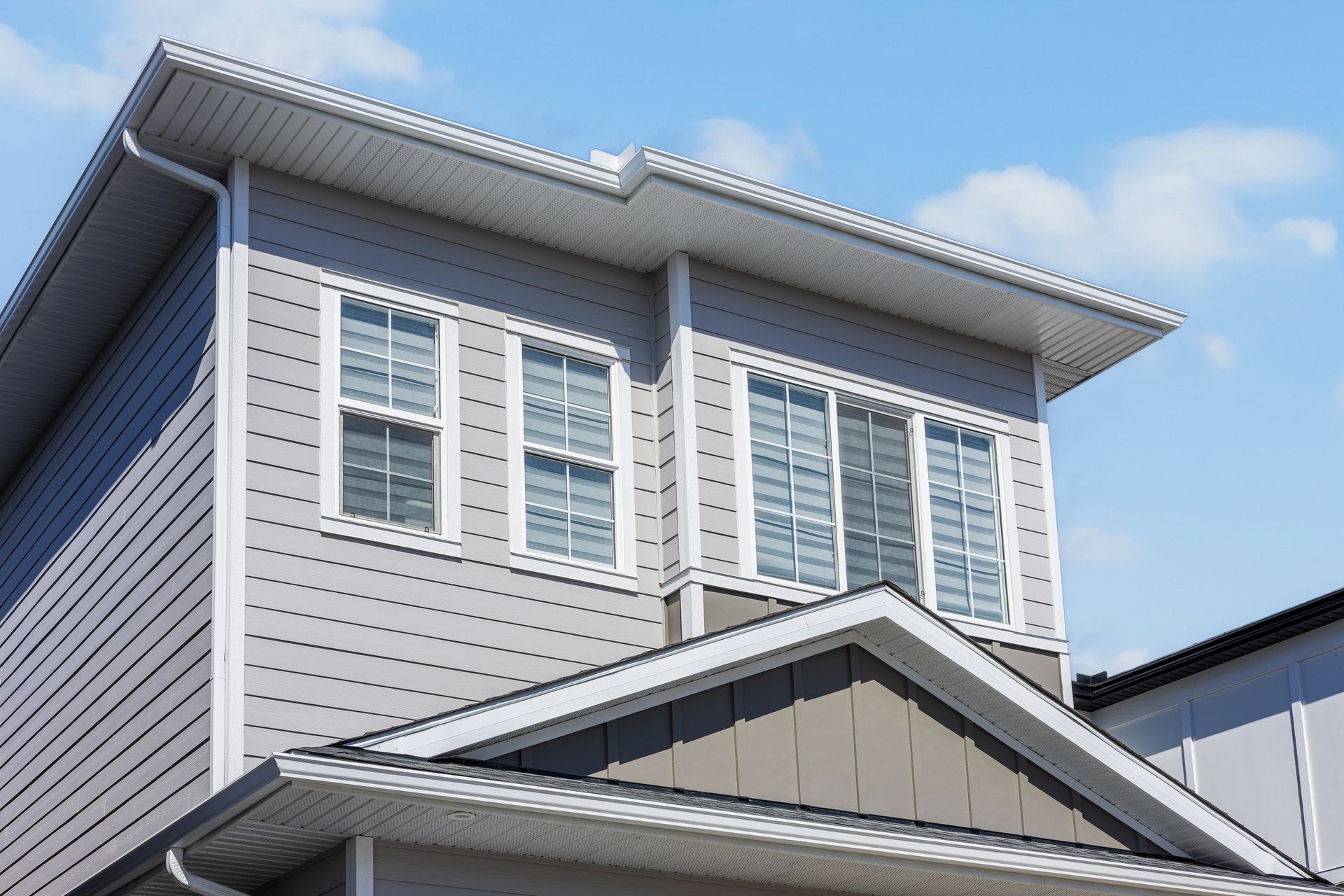 Two-story house with light gray siding, white-trim windows, and a blue sky background