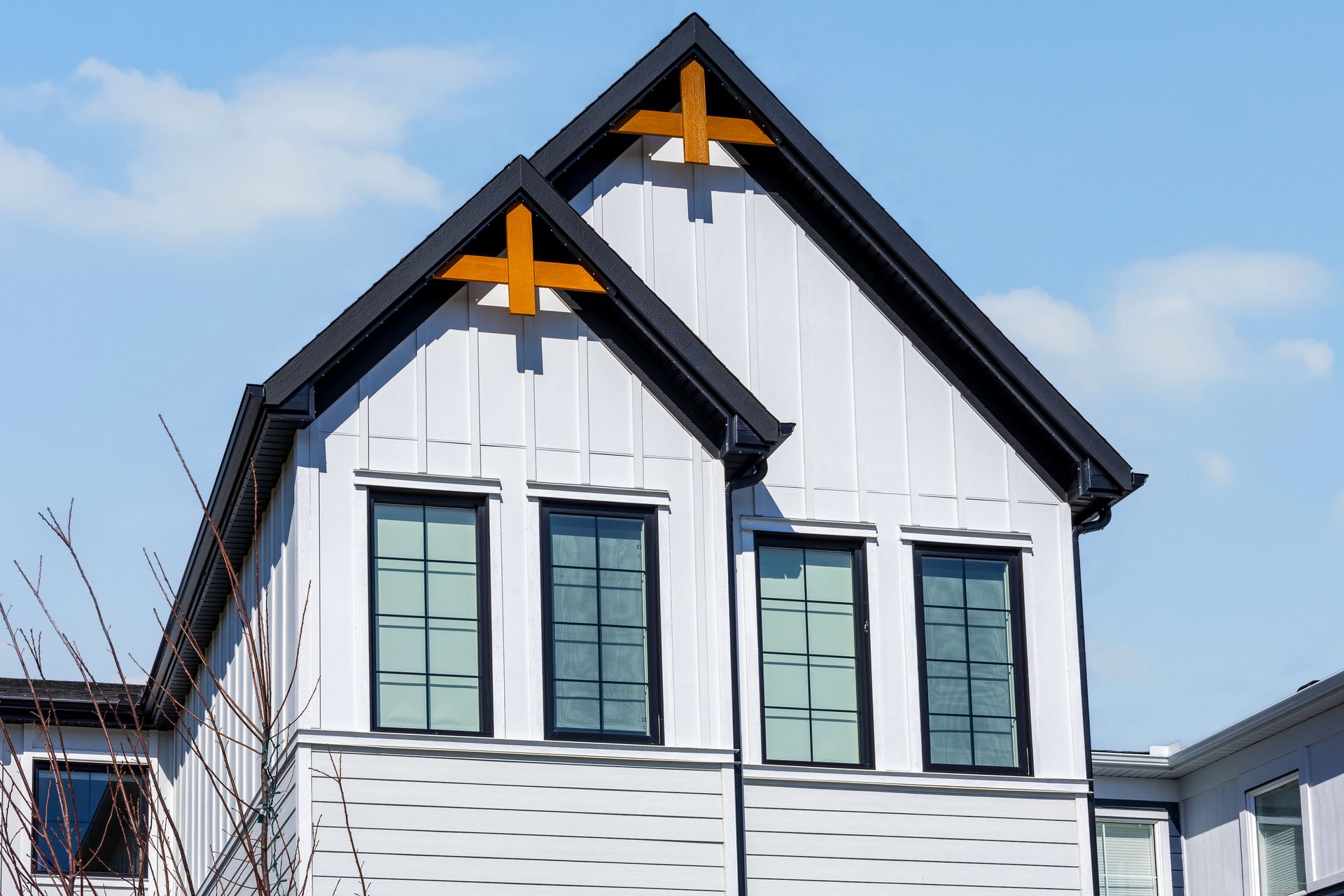 White building facade with black gabled roofs and orange cross accents against a blue sky