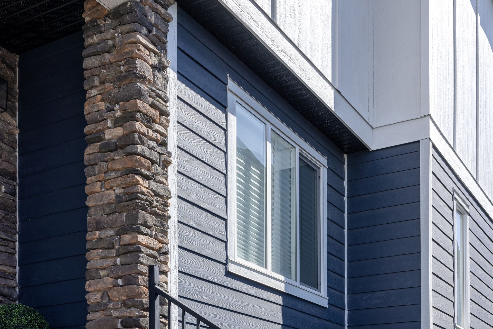 Modern house exterior with dark blue siding, stone column, and white-trimmed window
