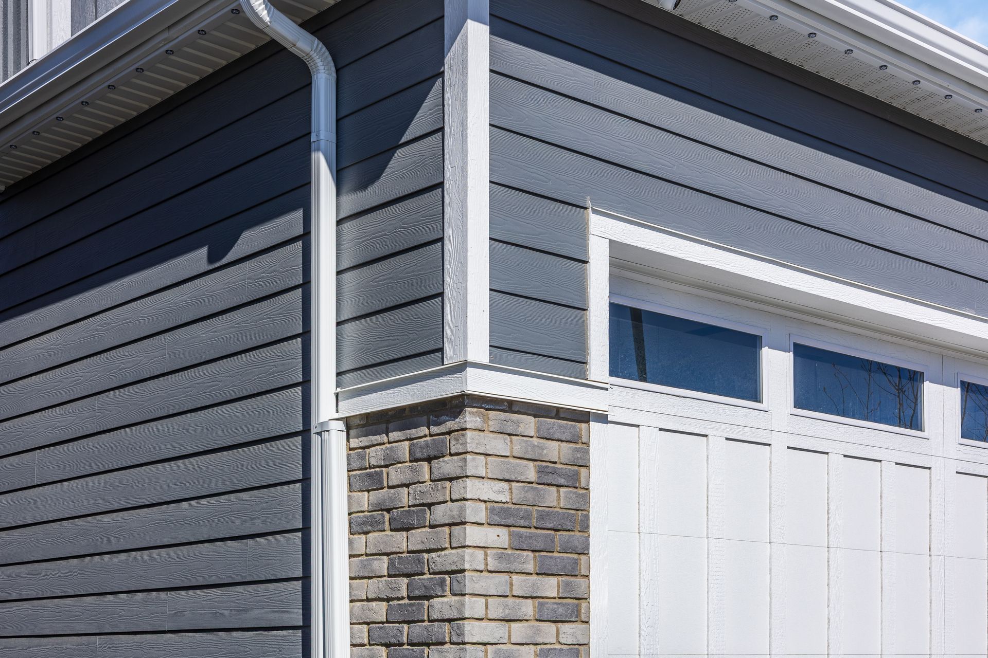 House exterior with dark gray siding, stone pillar, and white garage door beneath the eaves