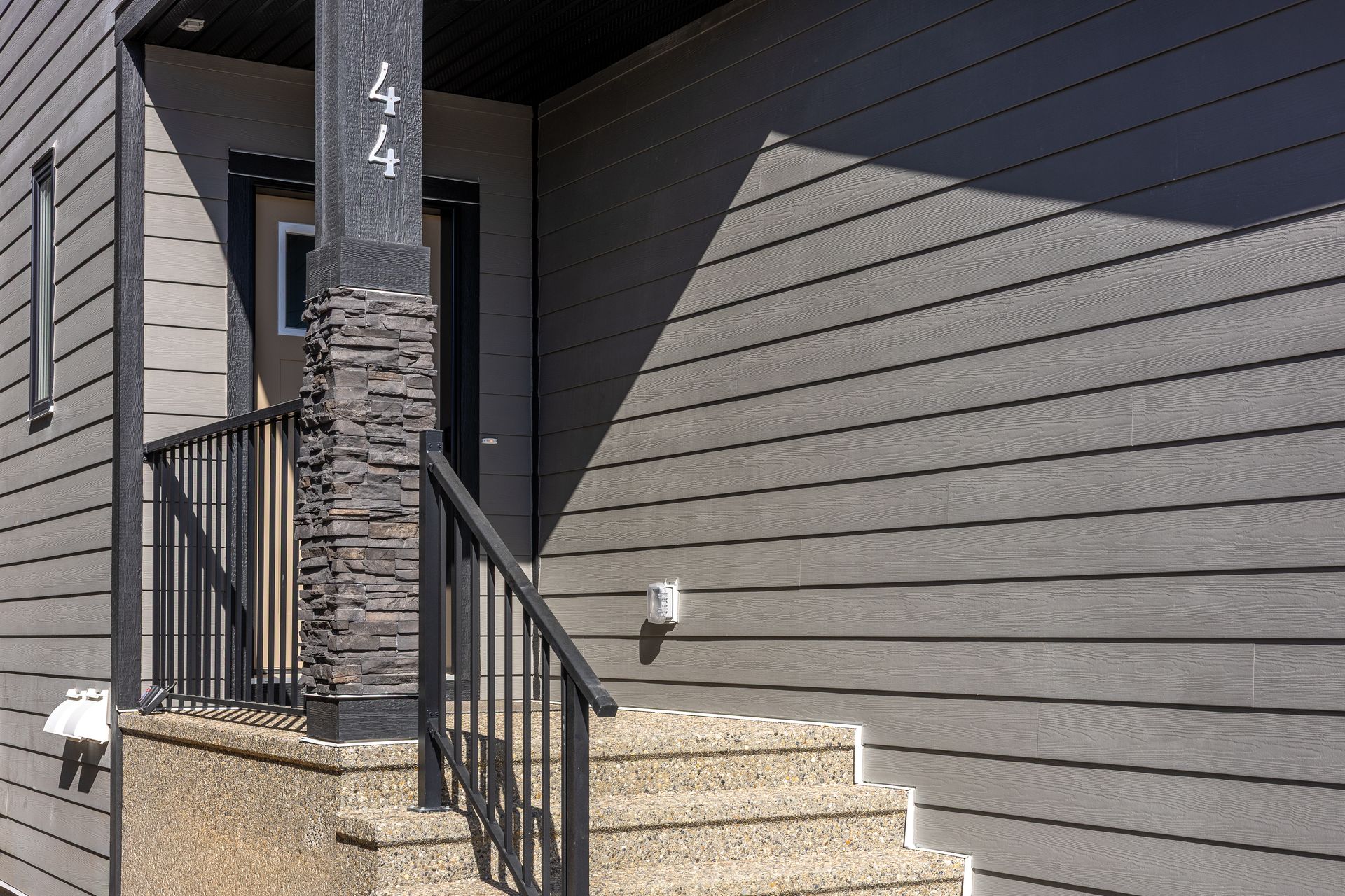 Front steps with metal railing leading to a gray house entrance beside a stone pillar marked 44