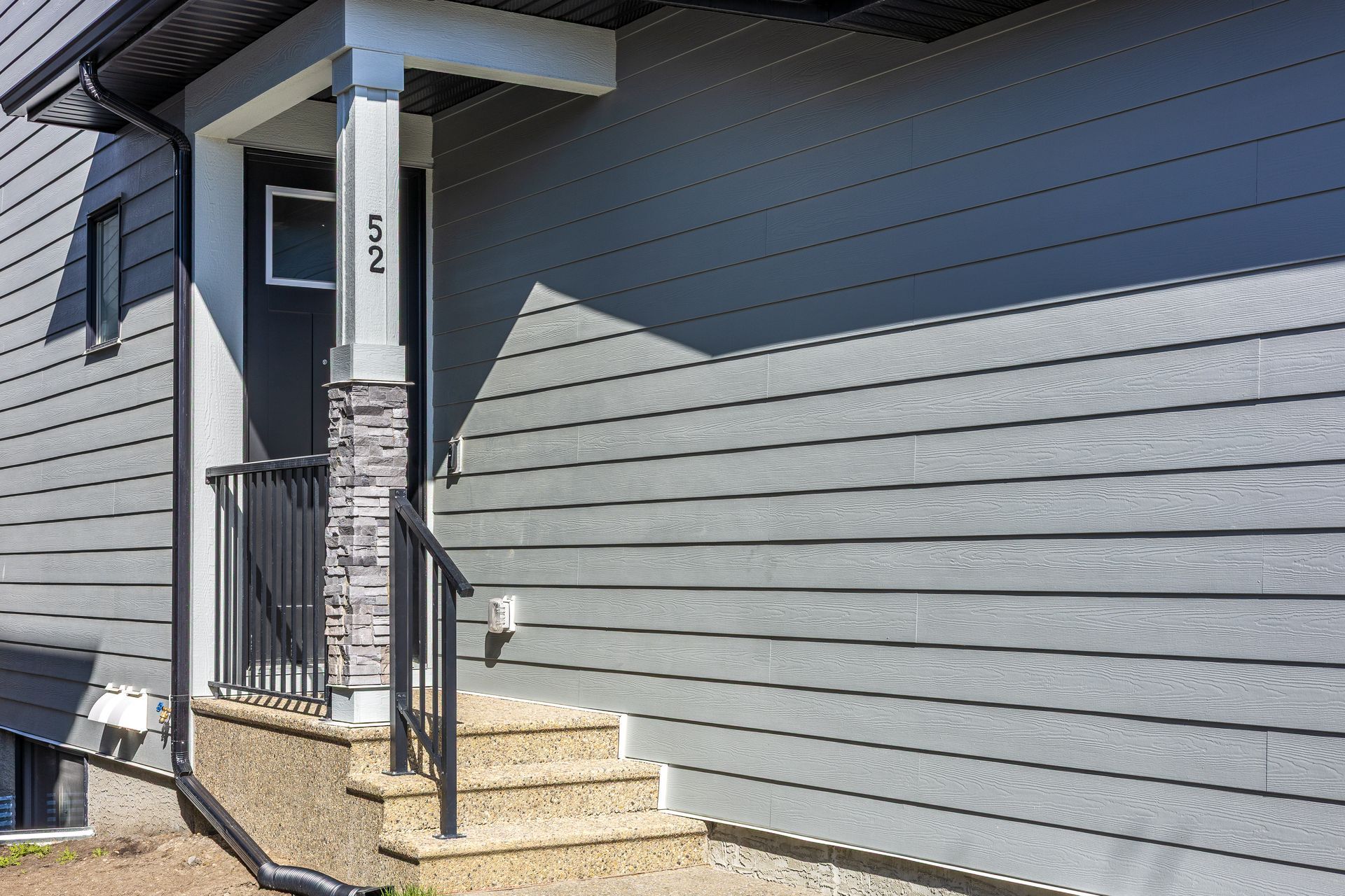 Gray house exterior with front steps, black railing, and a small porch under an awning