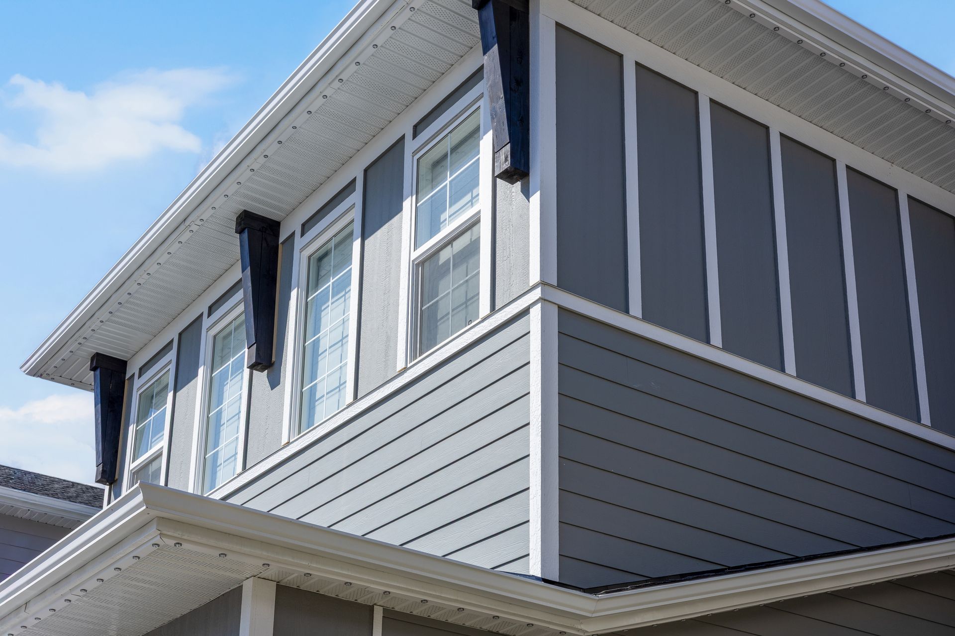 Corner of a two-story house with gray siding and white trim against a blue sky