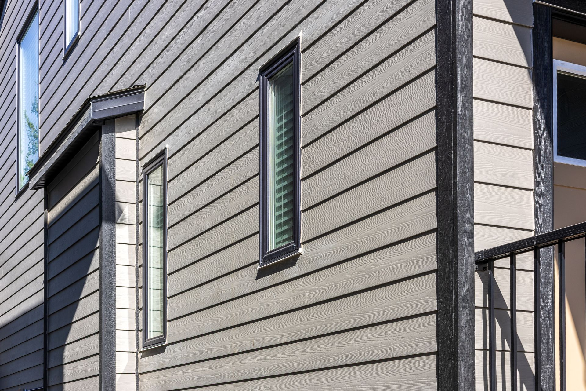 Gray house siding with narrow vertical windows and a balcony railing on the right