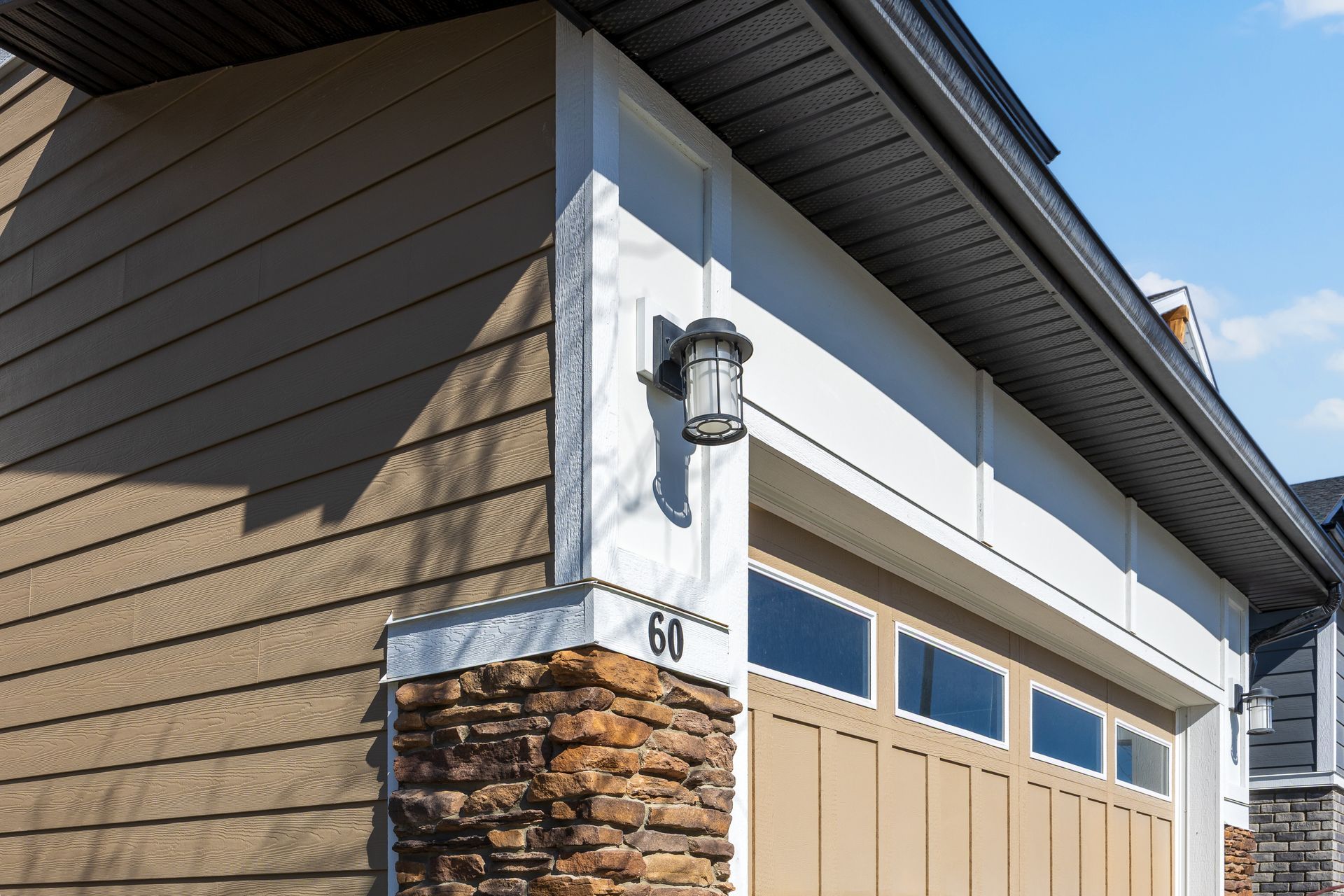 House corner with beige siding, stone accent, and a garage door under blue sky