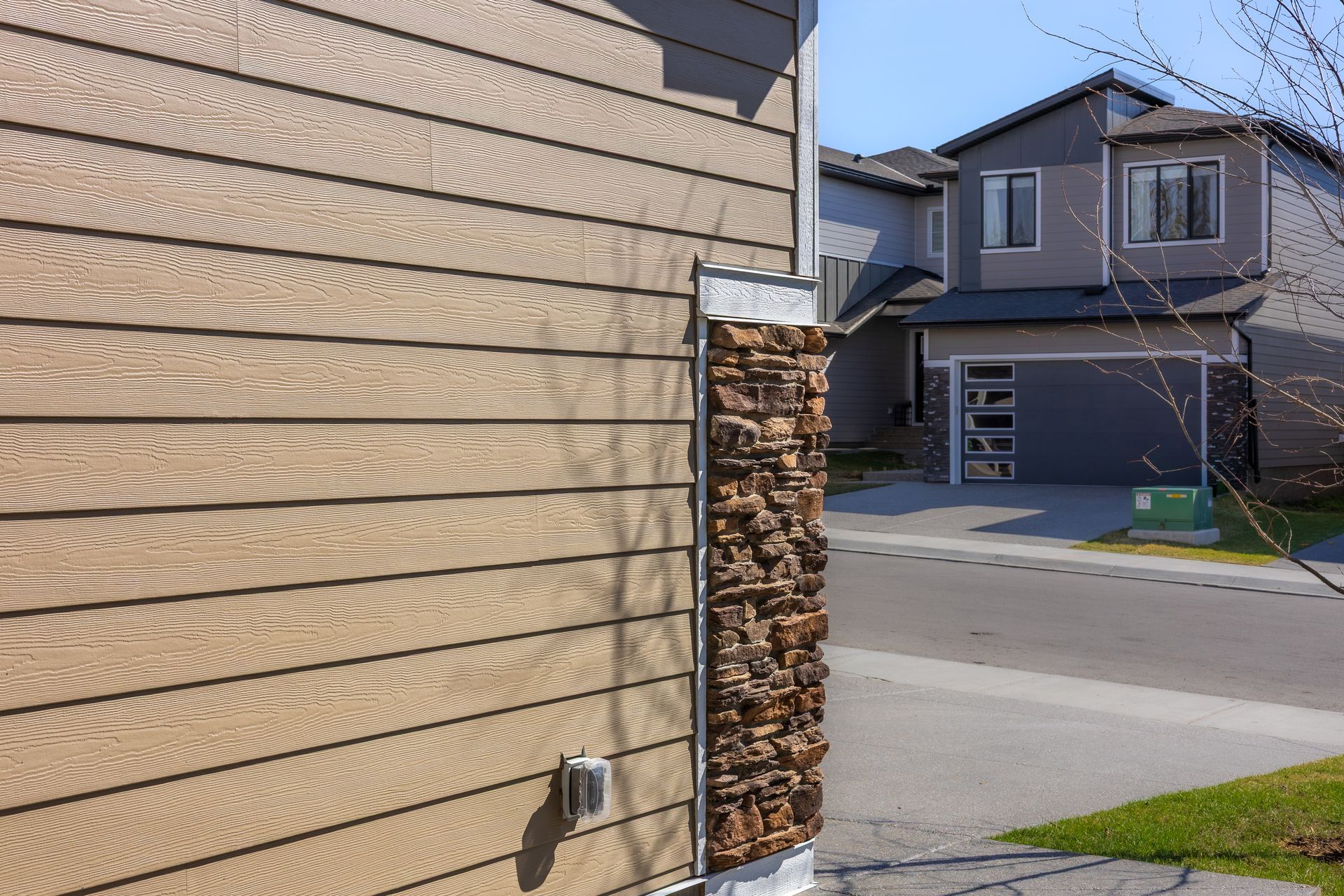 House exterior with tan siding, stacked firewood by the wall, and a suburban street with neighboring homes