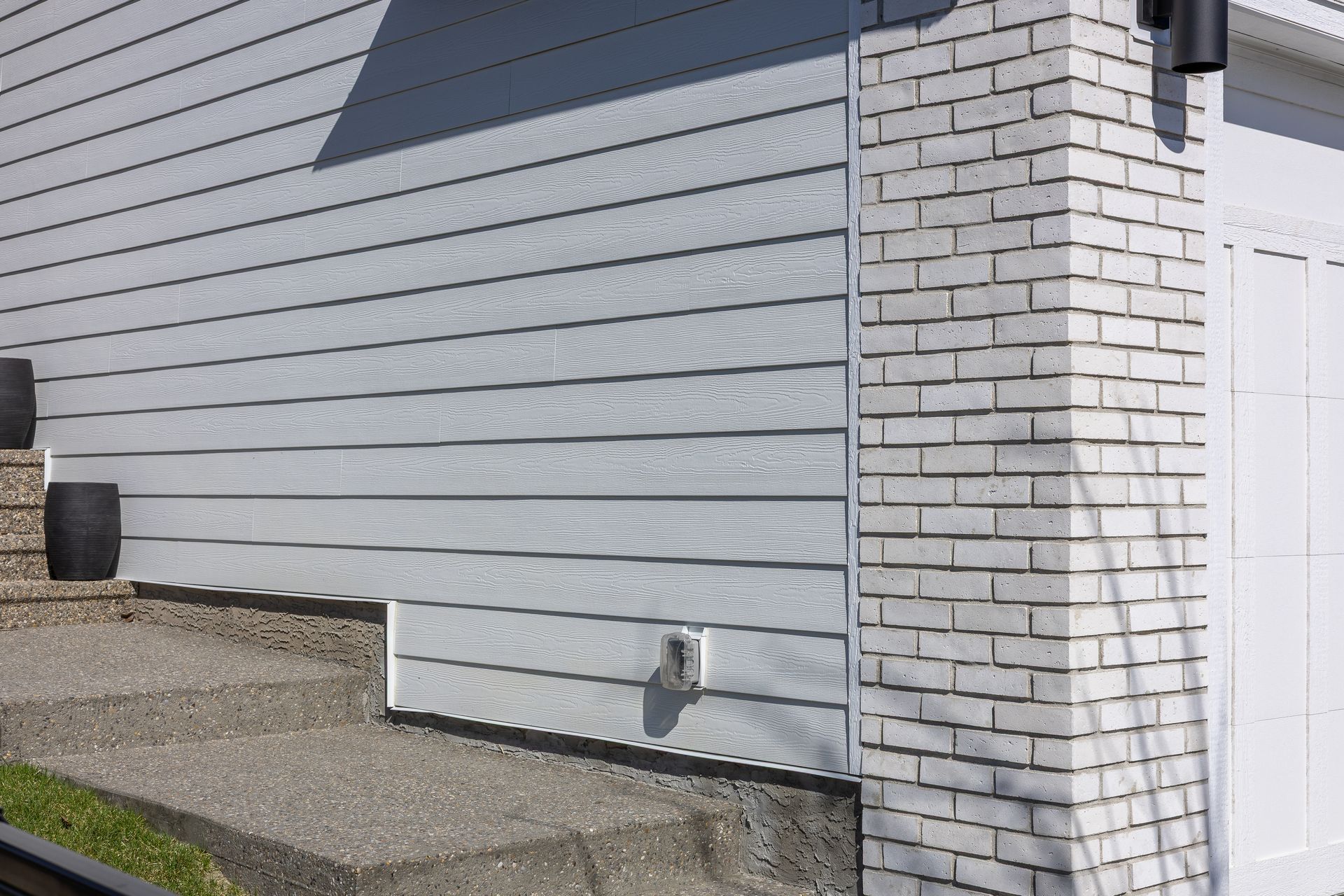 Gray house exterior with white brick corner, siding, and gravel ground beside a fence