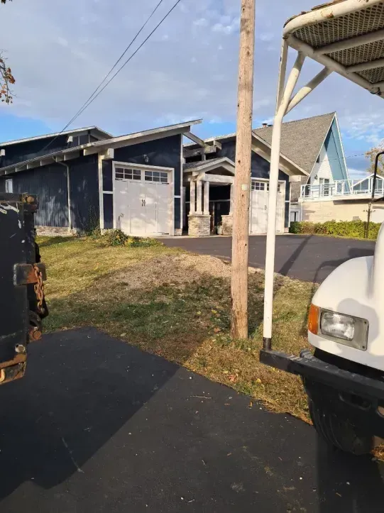 A view from a vehicle looking at a blue house with a two-car garage and a paved driveway, seen on a sunny day.