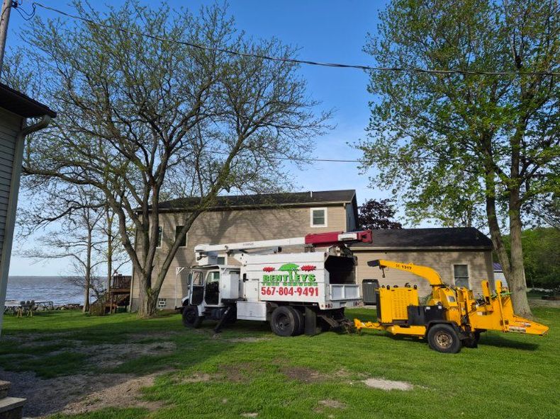 Tree service truck and wood chipper parked by a house under leafless trees near the water