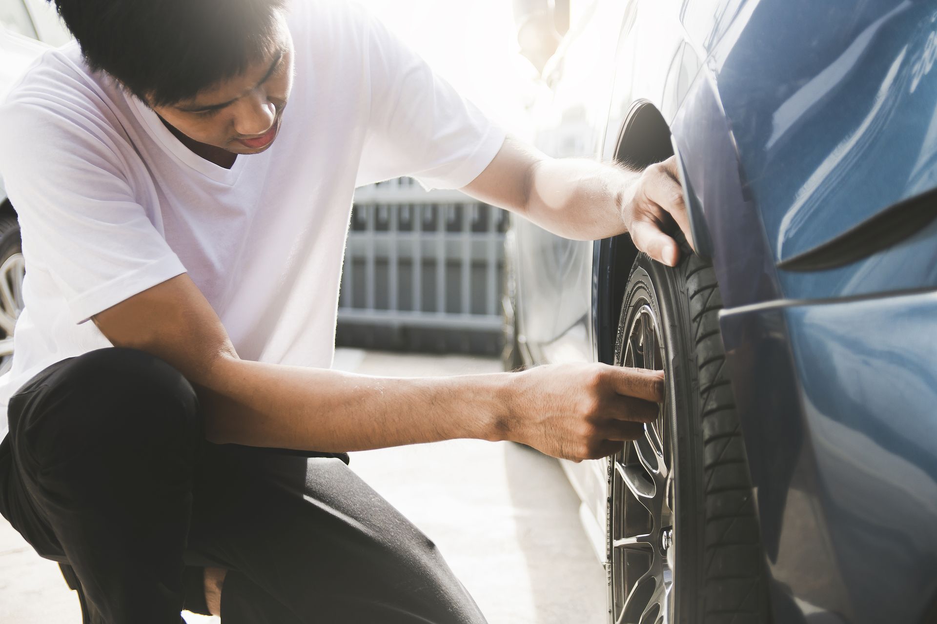 A man is kneeling down next to a car and checking the tire.