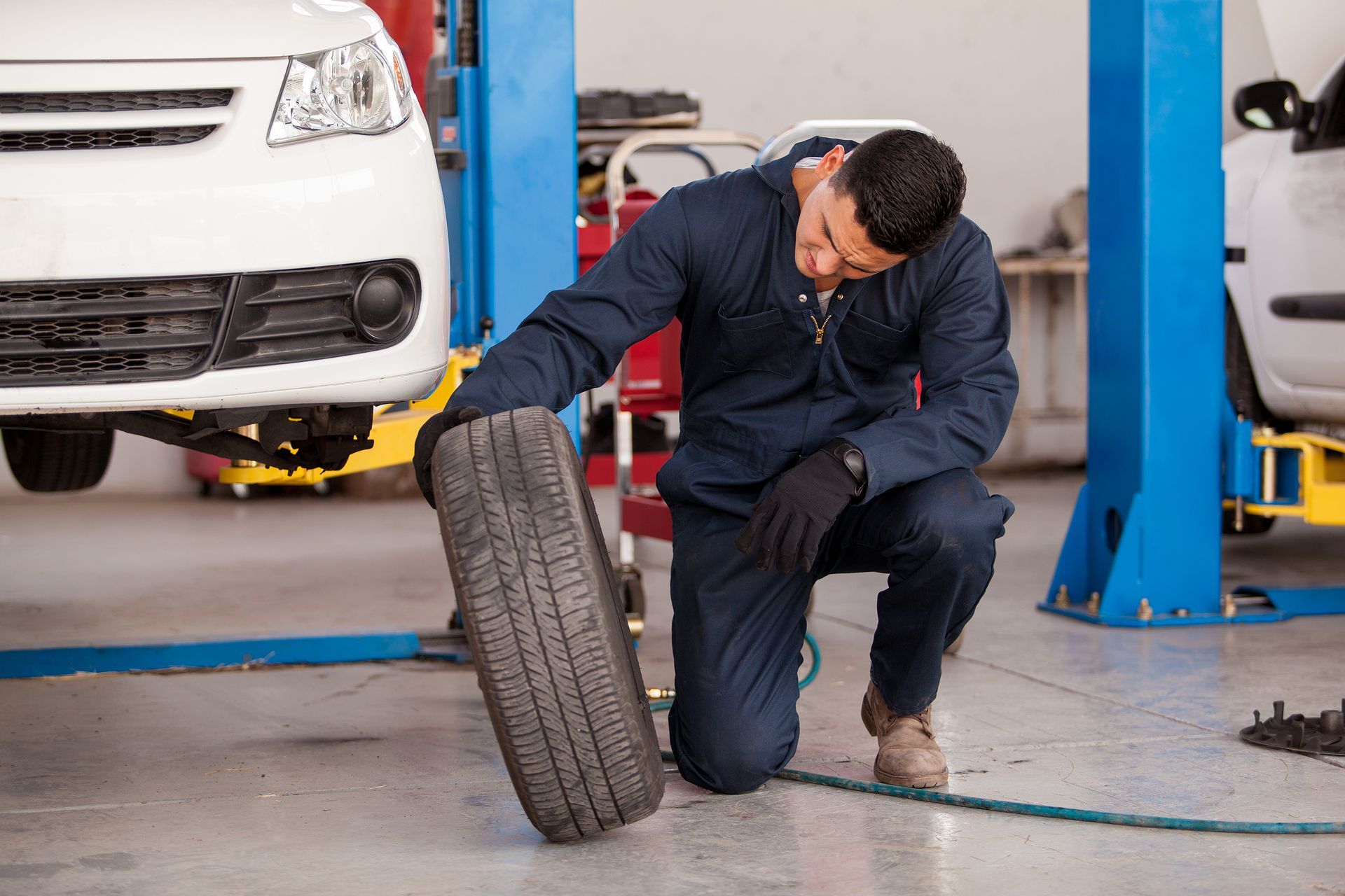 A man is kneeling down to change a tire in a garage.