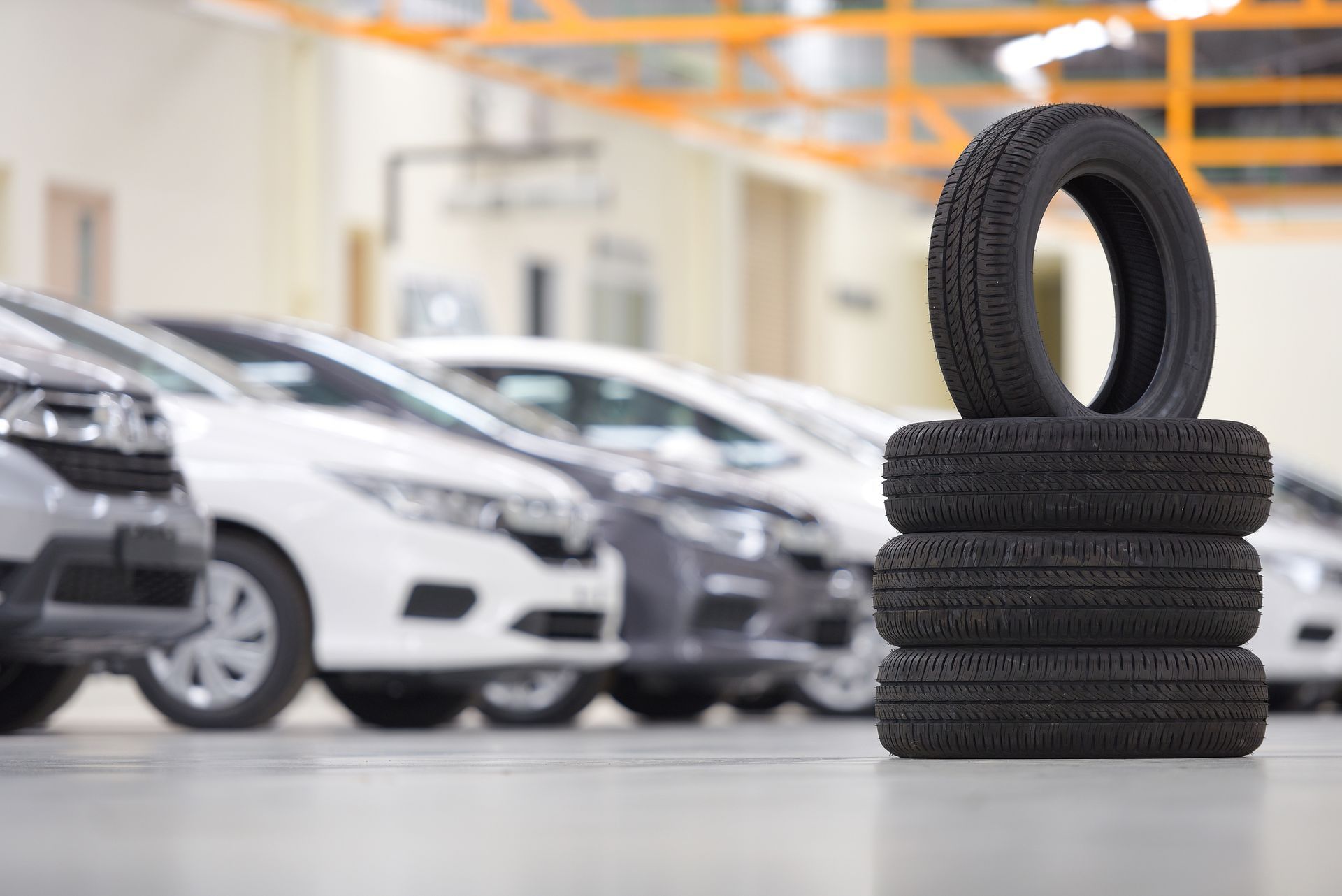 A stack of tires is sitting in front of a row of cars in a garage.