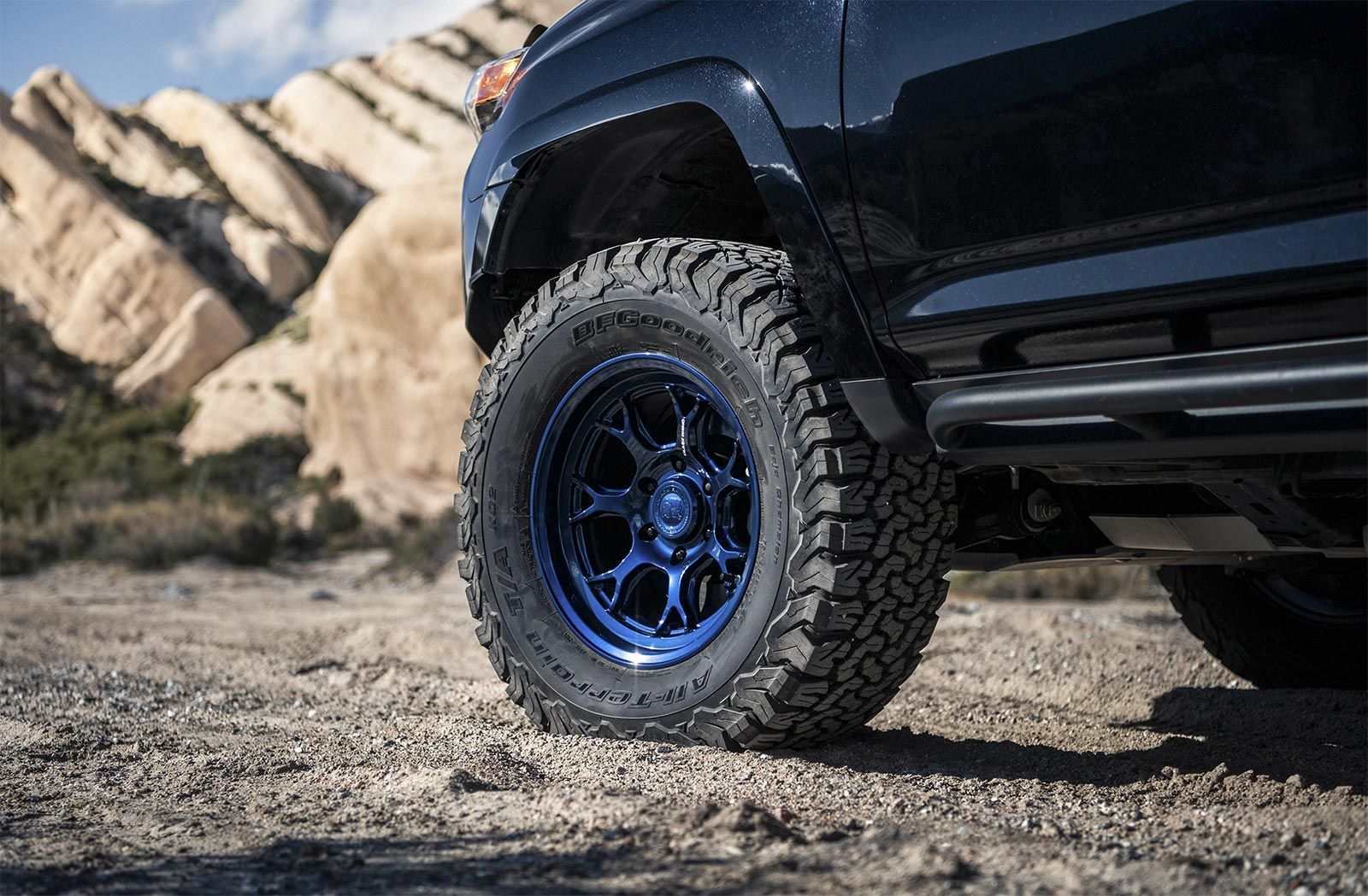 A black truck with blue tires is parked in the dirt