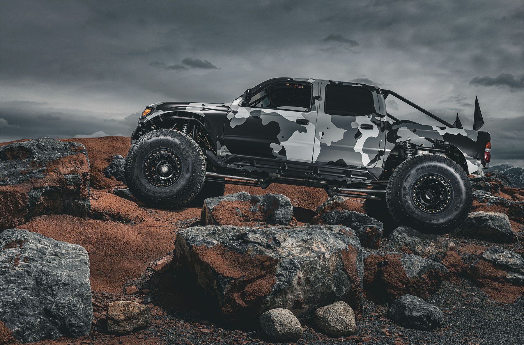 A black and white camouflage truck is parked on top of a rocky hill.