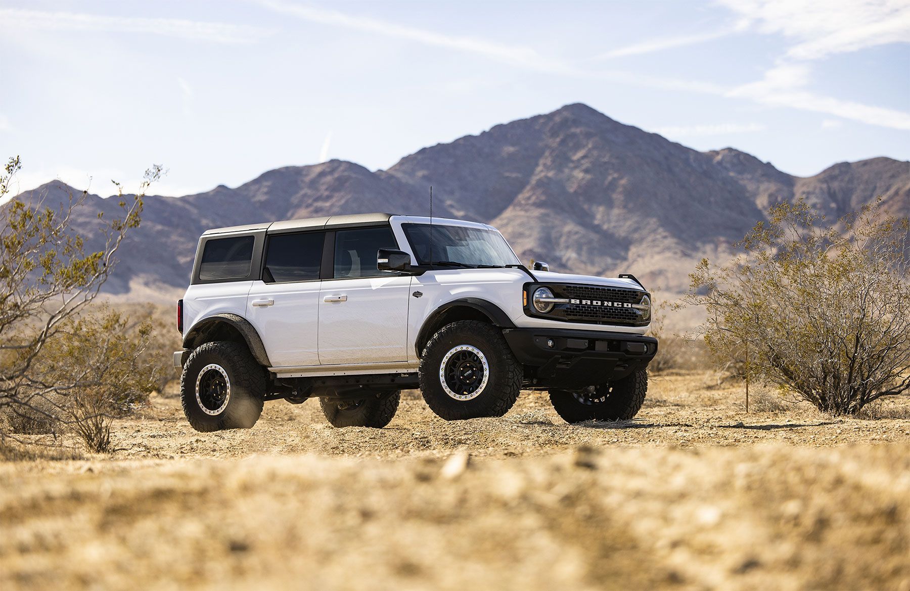 A white suv is parked in the desert with mountains in the background