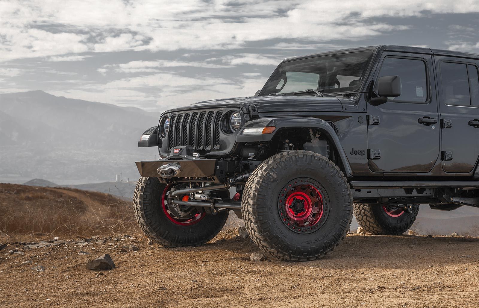 A black jeep with red wheels is parked on a dirt road.