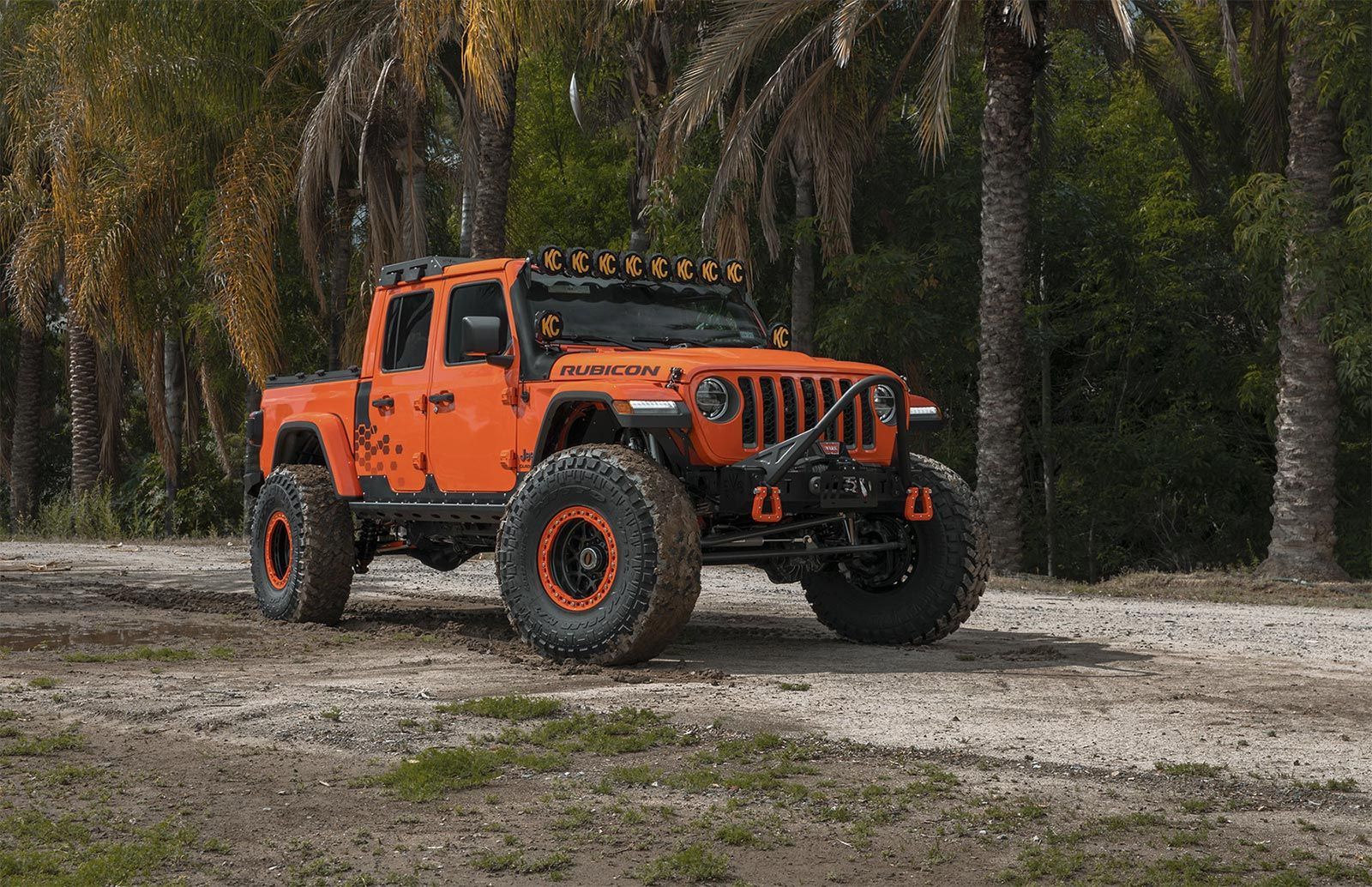 An orange jeep is parked on a dirt road in the woods.