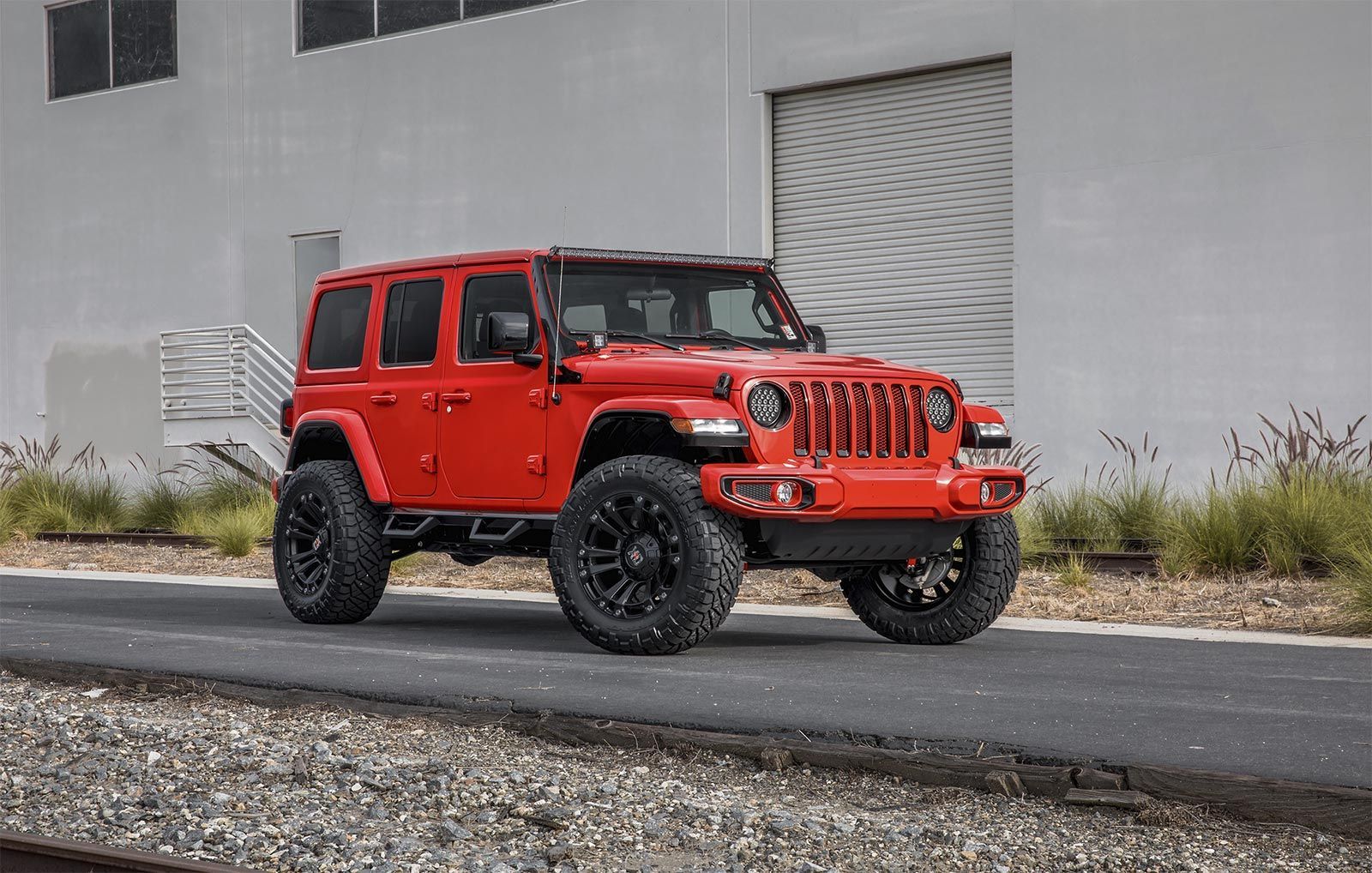 A red jeep is parked on the side of the road in front of a building.