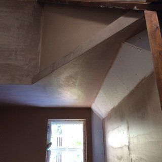 Interior room under renovation; angled walls and ceiling with applied plaster. Window at bottom.
