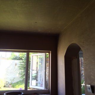 Interior view of a room with a large window, open door frame, and finished plaster walls.