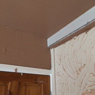 Brown ceiling meeting a plaster wall with a white trim, and a wooden door.
