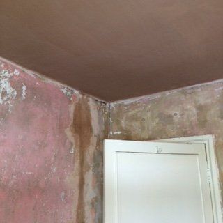 Corner of a room with pink and brown walls, a brown ceiling, and a white door. Water damage is visible.