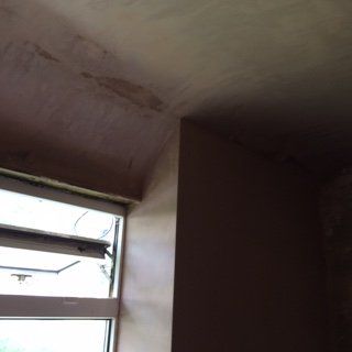 Room interior with unfinished plasterwork near a window. Beige walls and ceiling with some damage.