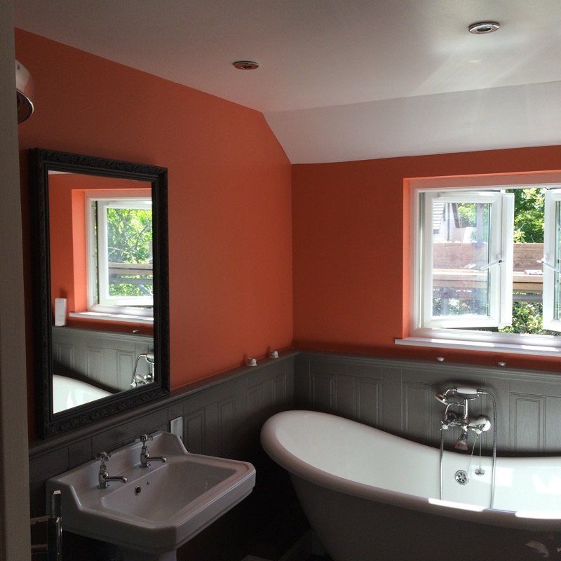 Bathroom with orange walls, white ceiling, clawfoot tub, sink, and two windows.