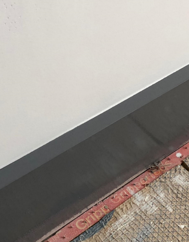 Gray wall with a dark gray baseboard, next to a textured, red-edged surface.