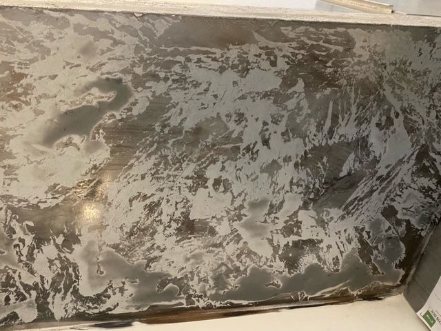 Textured gray and silver surface, possibly metallic, with irregular patterns and varying light reflection.