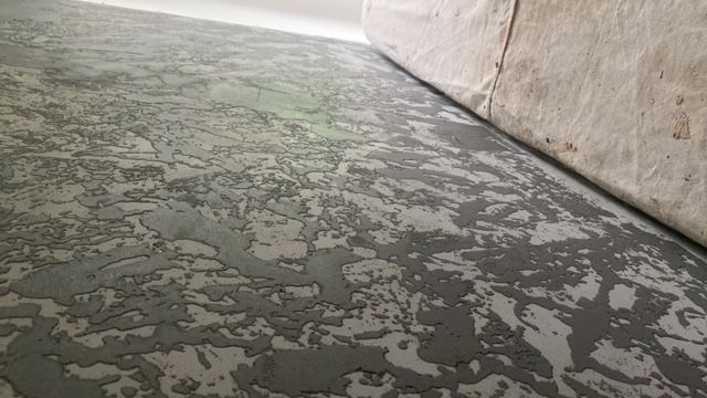 Textured gray and white surface, possibly flooring or a wall, next to a rolled-up, beige material.