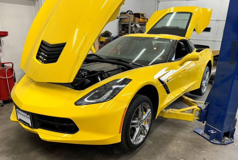 Yellow Corvette sports car on a lift with hood and doors open inside a garage. | Beach Auto Repair