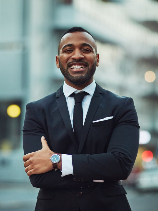 A man in a suit and tie is smiling with his arms crossed