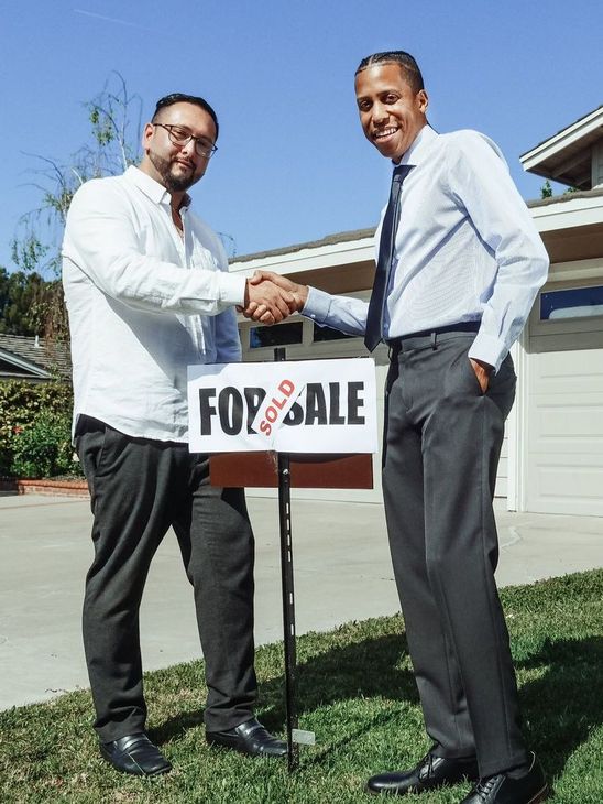 Two men shaking hands in front of a for sale sign