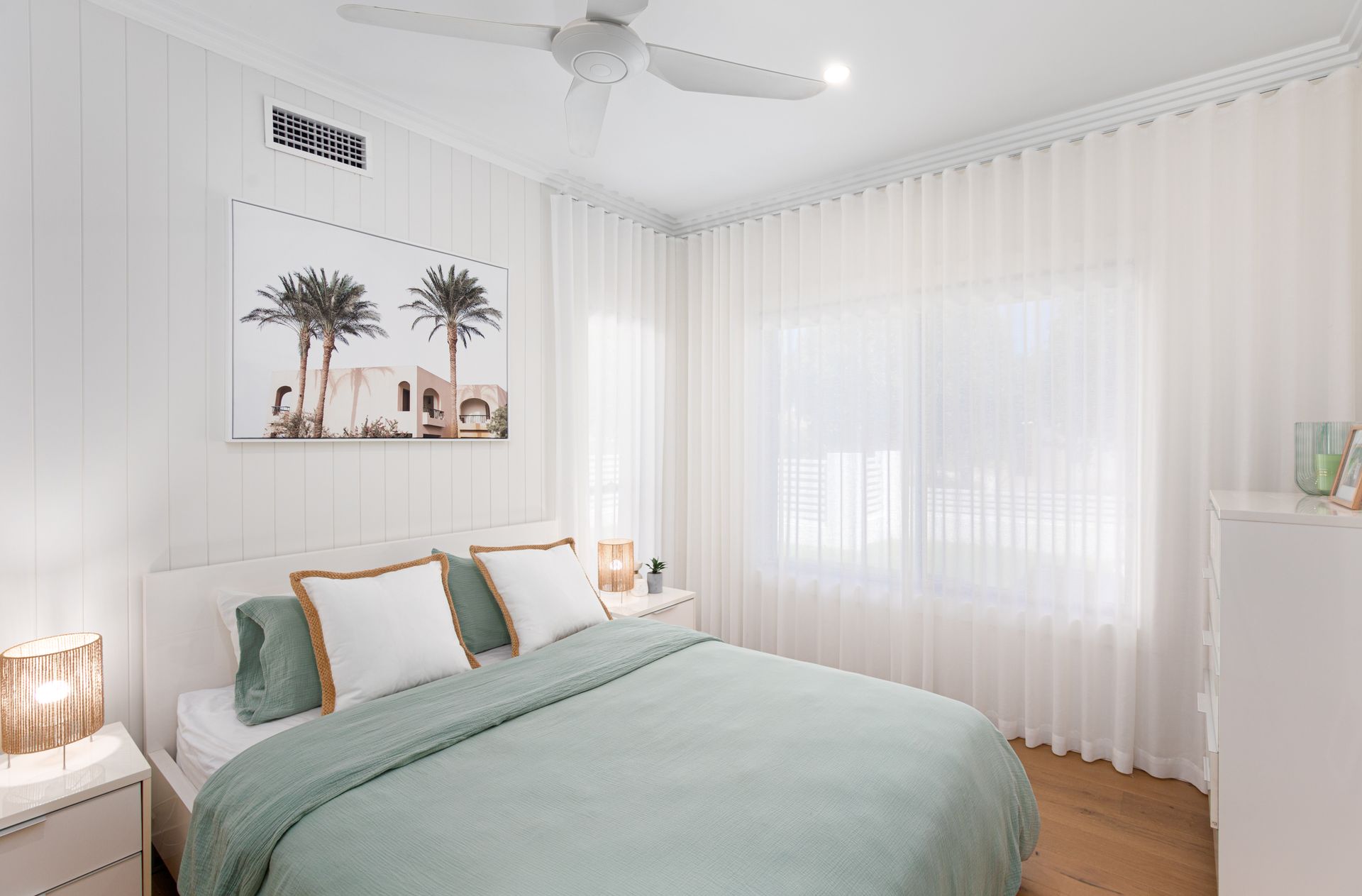 A bedroom with a bed , nightstand , ceiling fan and white curtains.