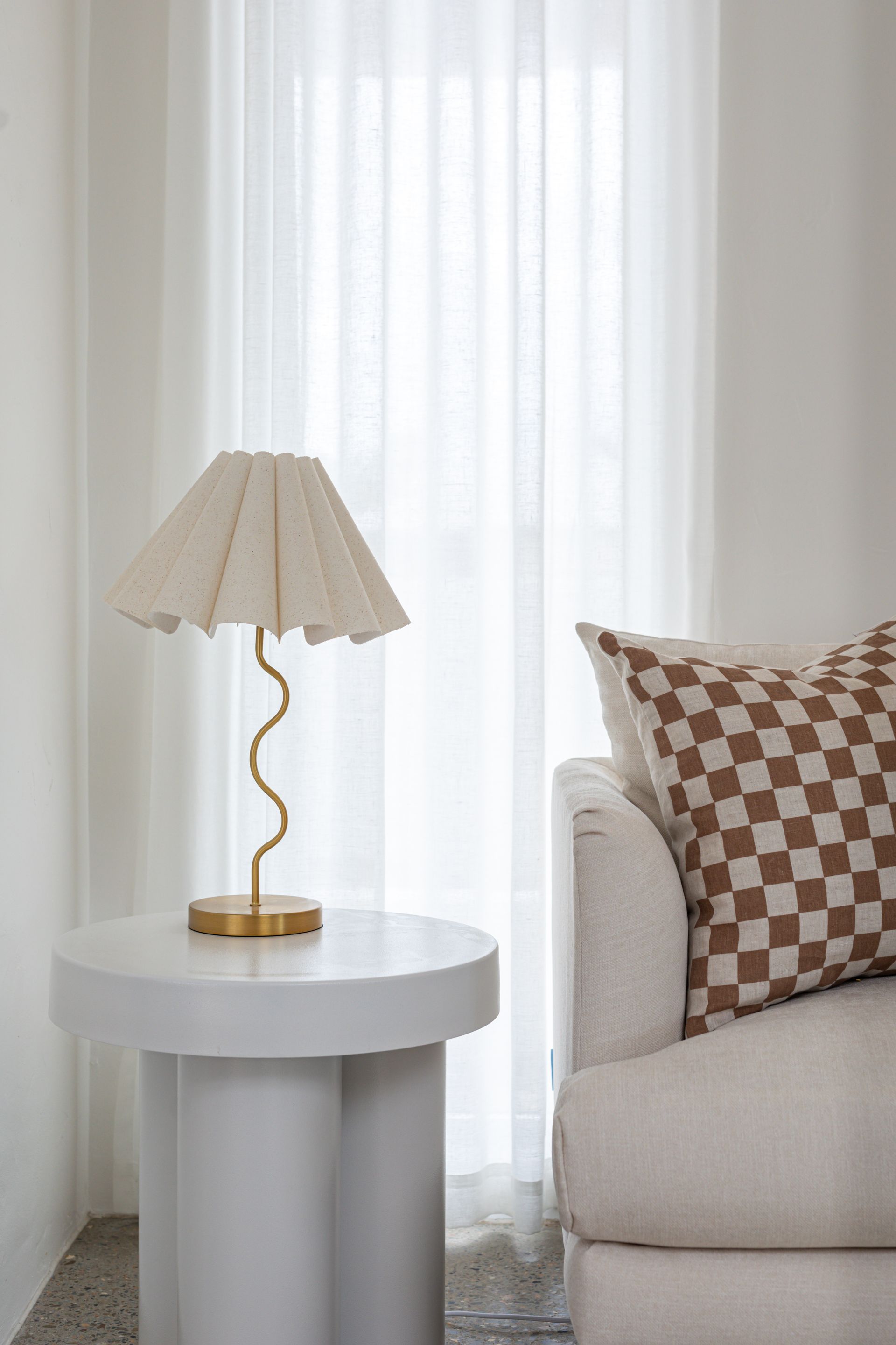 A lamp is sitting on a white table next to a couch.