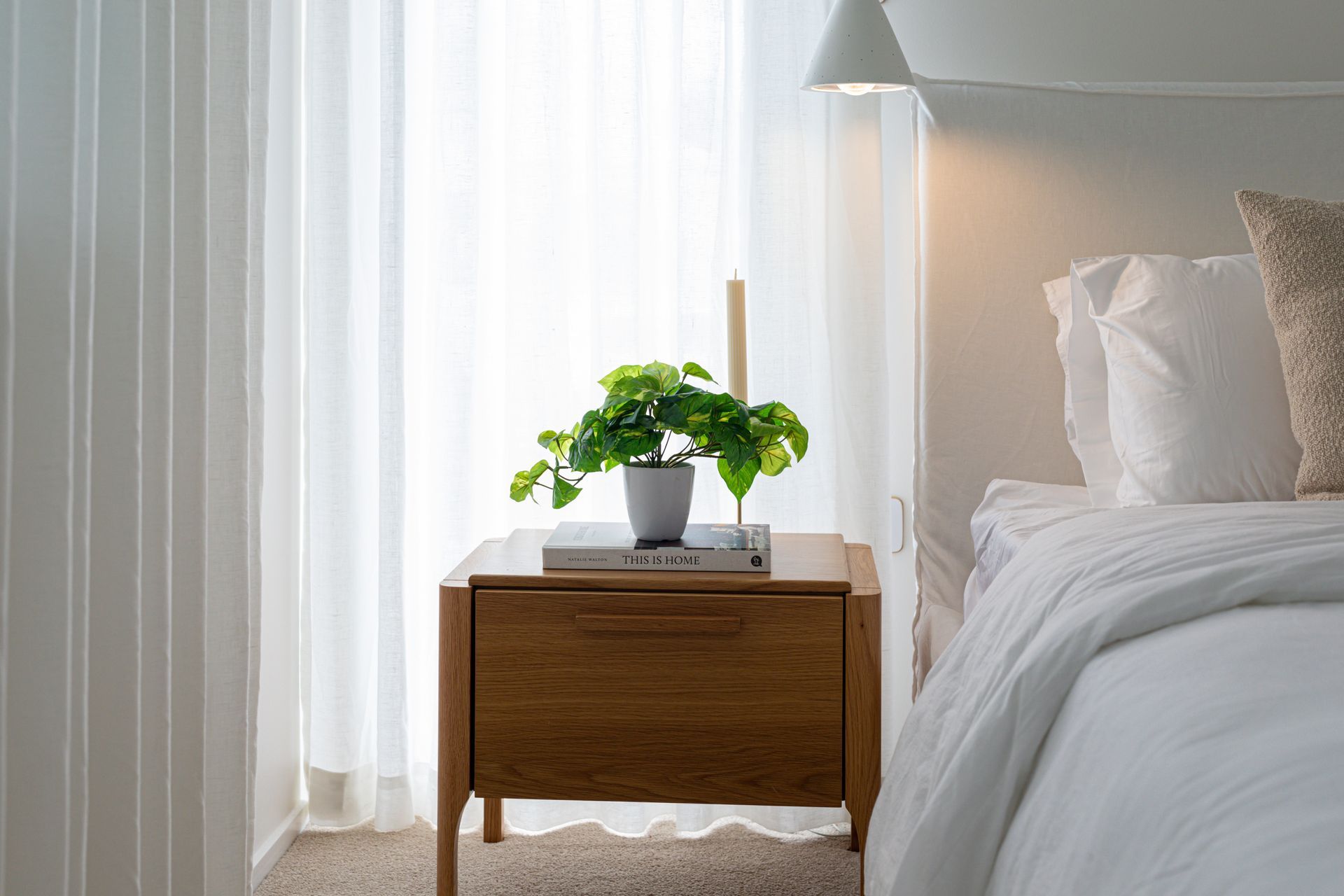 A bedroom with a bed and a nightstand with a plant on it.