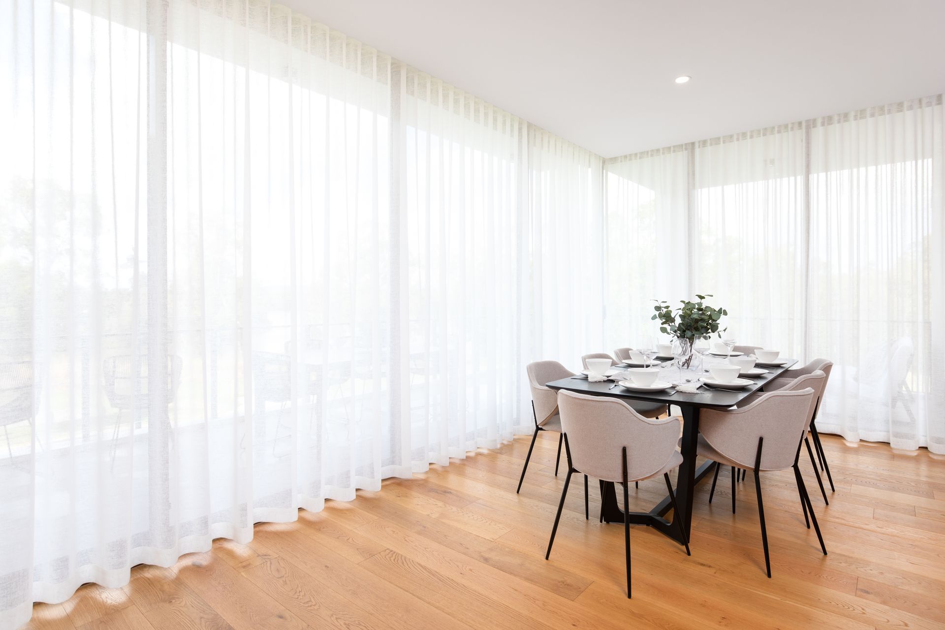 A dining room with a table and chairs and white curtains.
