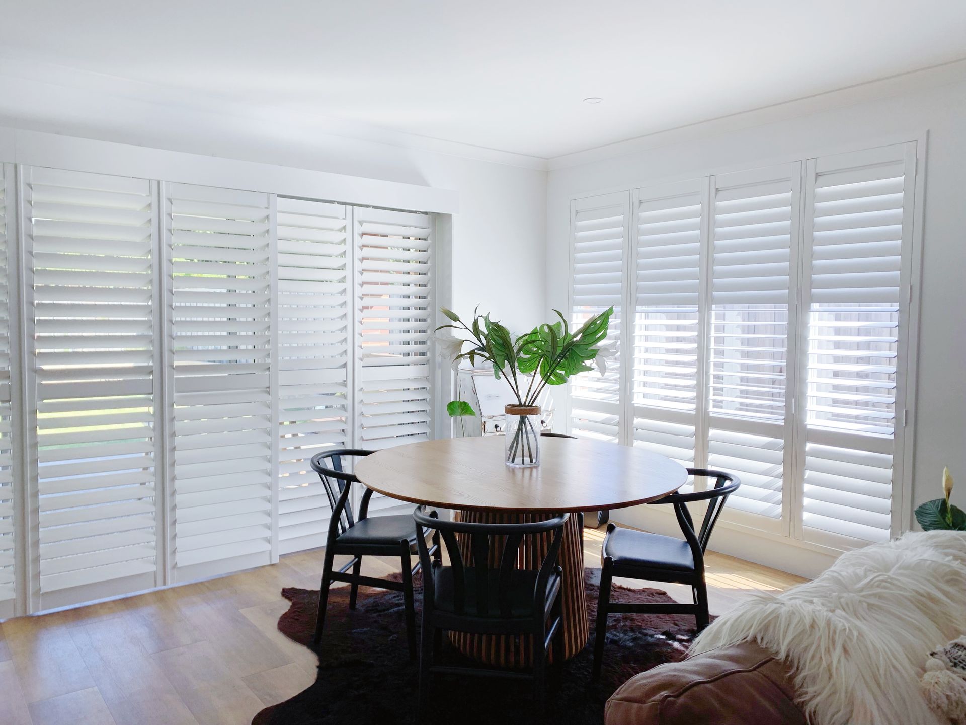 A dining room with a table and chairs and shutters on the windows.