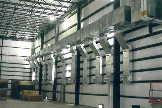 A large warehouse with a lot of pipes hanging from the walls.