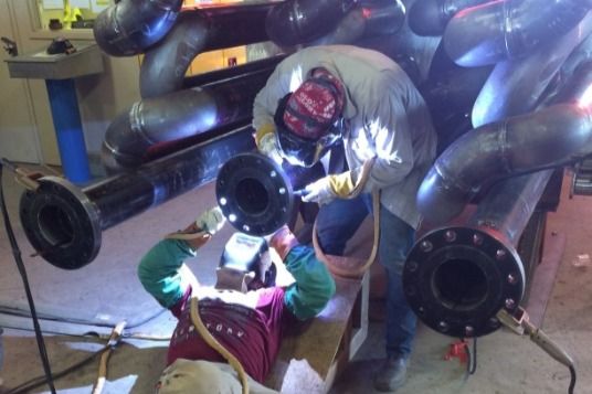 Two men are welding pipes together in a factory