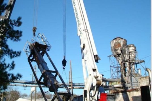 A large white crane is lifting a large pipe