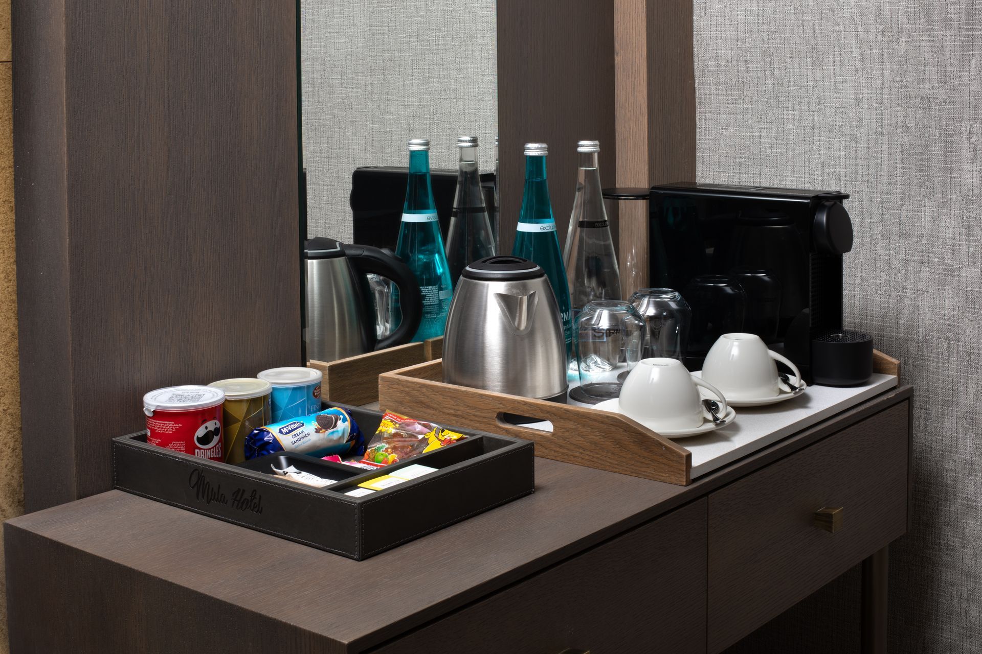Mula Hotel | Hotel coffee and beverage station on a counter with water bottles, coffee cups, and snacks.