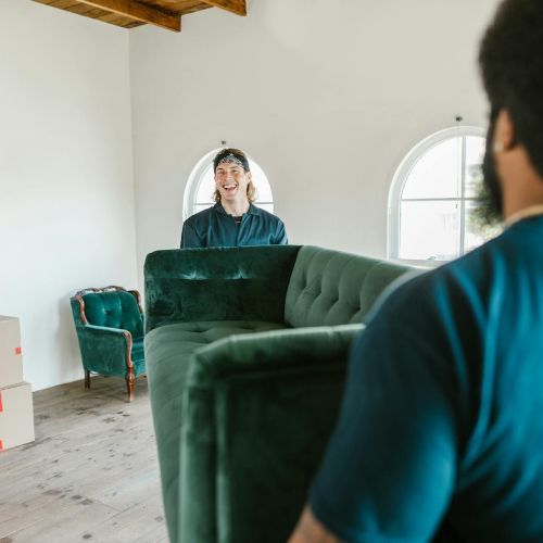 A man is moving a green couch in a living room.