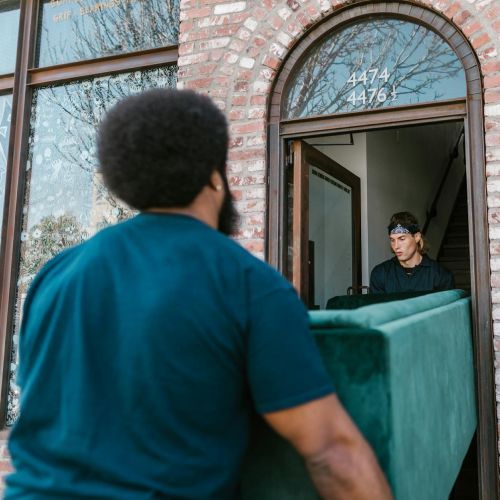 A man is carrying a green couch into a house.