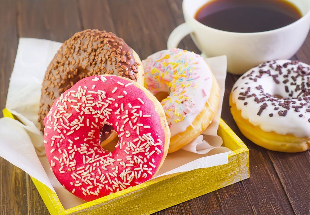 three donuts in a yellow tray next to a cup of coffee