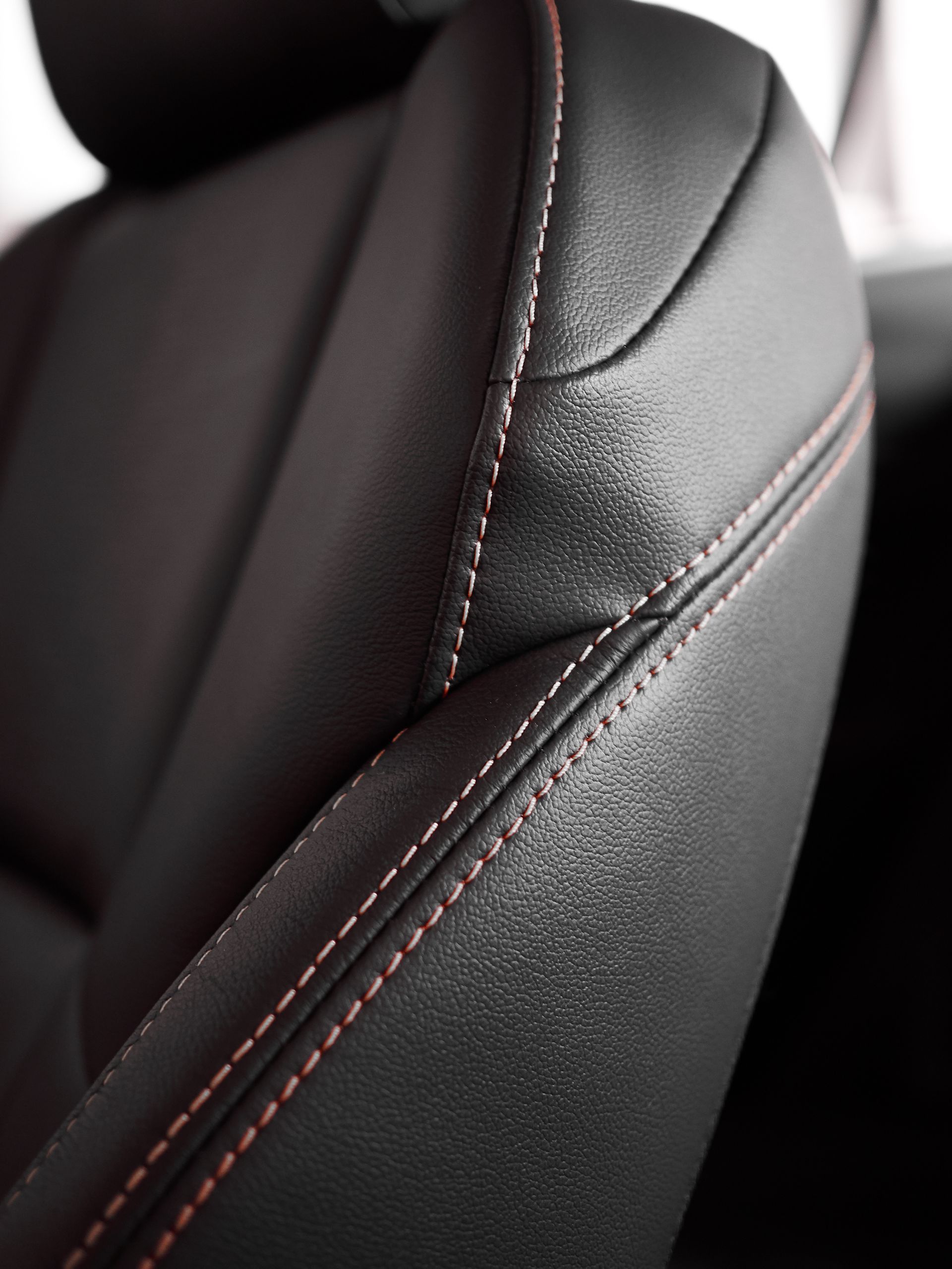 Close-up of a dark leather car seat featuring textured upholstery and contrasting red stitching along the seams.